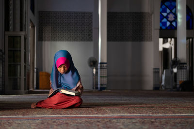 Girl in hijab reading book while sitting at mosque