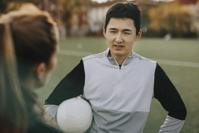Male athlete talking with female coach while standing in sports field