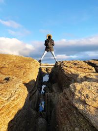 Full length of man standing on rock formation against blue sky