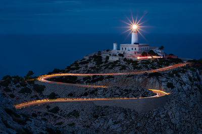 Illuminated building by sea against sky at night