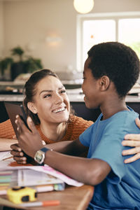 Happy mother talking to son holding digital tablet at home