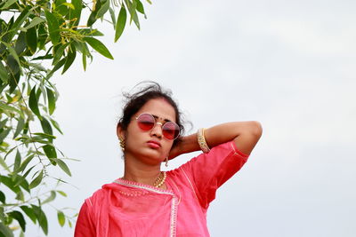 Portrait of young woman wearing sunglasses standing against sky