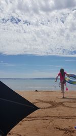 Rear view full length of girl with inflatable ring walking at beach