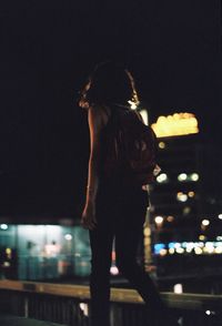 Side view of woman standing against illuminated city at night
