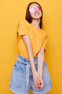 Portrait of young woman standing against yellow background