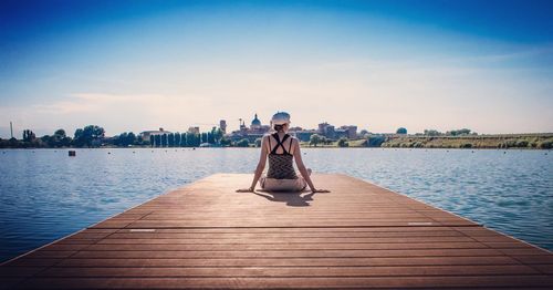 Woman sitting on pier over lake against sky