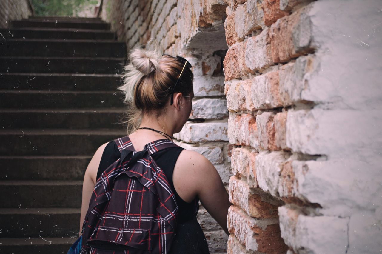 one person, real people, wall, wall - building feature, standing, brick wall, brick, lifestyles, architecture, casual clothing, women, built structure, leisure activity, waist up, hairstyle, rear view, young adult, staircase, hair, stone wall, outdoors, teenager