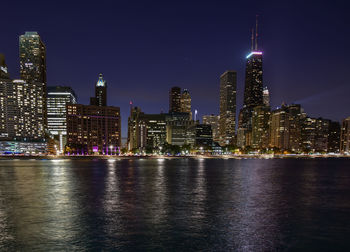 Illuminated modern buildings against clear sky by river