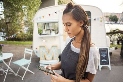 Female owner using mobile phone on street against food truck