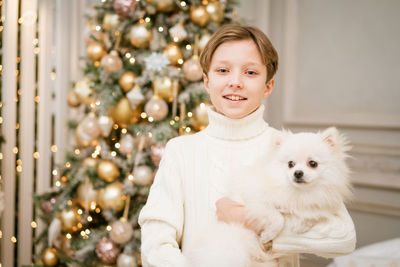 Cute boy at christmas tree with dog in anticipation of