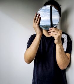 Midsection of man holding umbrella standing against wall