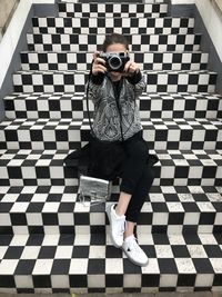 Full length of woman photographing while sitting on tiled staircase