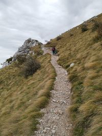 Rear view of people climbing mountain against sky