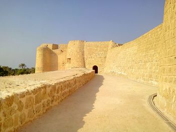 Walkway leading towards fort against clear sky on sunny day