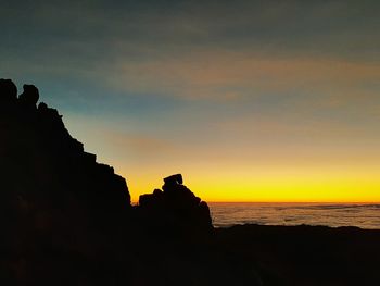 Silhouette rock formations by sea against sky during sunset