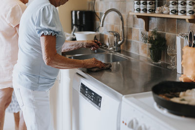 Mid section of senior woman cleaning worktop in kitchen