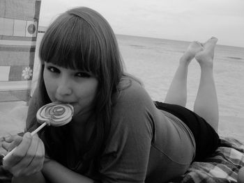 Portrait of woman eating lollipop while relaxing at beach