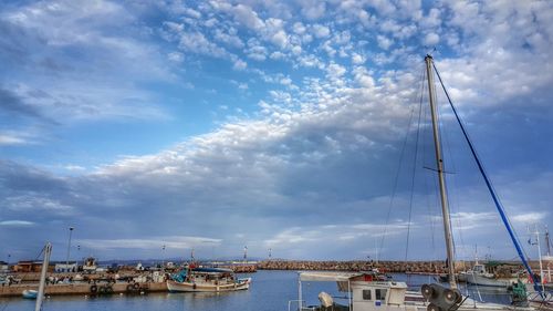 Boats in harbor against cloudy sky