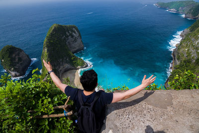 Rear view of man with arms outstretched sitting against sea