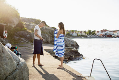 Full length of couple wrapping themselves in towel at lakeshore