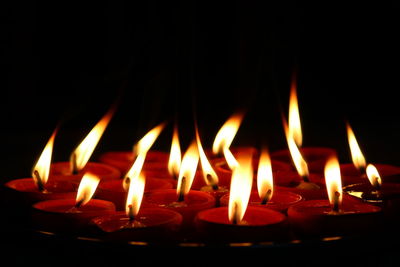 Close-up of burning candles against black background