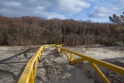 Yellow railing on snow covered land against sky