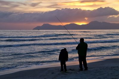 Rear view of silhouette man fishing at beach during sunset