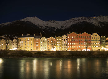 Illuminated buildings by mountains against sky at night