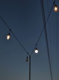 Low angle view of light bulb hanging on cable under sky