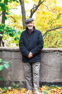 Portrait of happy senior man standing with hands clasped in park during autumn