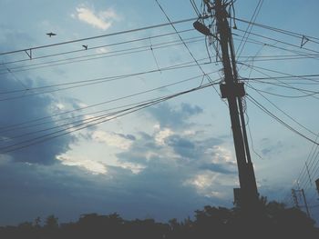 Low angle view of electricity pylon against cloudy sky