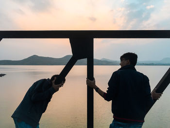 Men standing by sea against sky during sunset