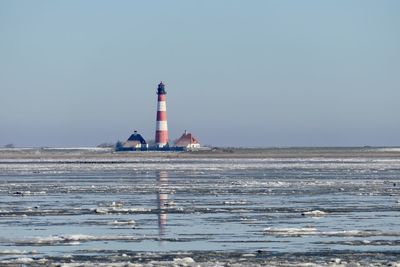 Lighthouse by sea against clear sky