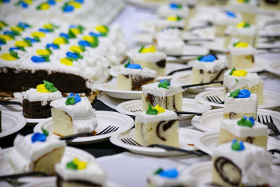 Many dessert plates of cake slices on paper plates with plastic forks sitting near the large cake.