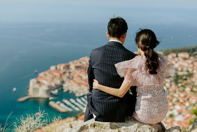Rear view of married couple sitting on rock against sea