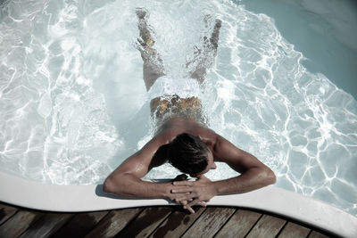 Rear view of young man relaxing in swimming pool