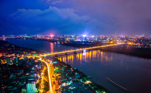 Illuminated city by river against sky at night