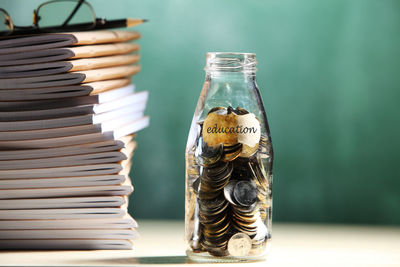 Stack of books with coins at classroom against blackboard