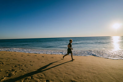 Full length of man running on beach against clear sky