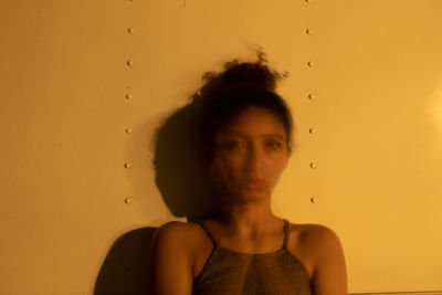 Portrait of young woman looking away against orange wall