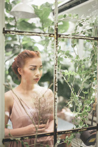 Young woman holding plant seen through glass window