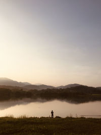 Man standing on field by lake against sky