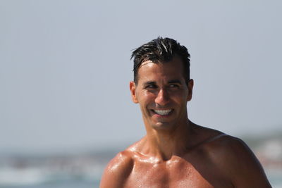 Portrait of shirtless man smiling at beach against clear sky