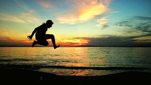 Silhouette of person jumping on beach against sky