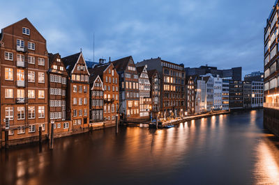 Buildings by river against sky in city at dusk