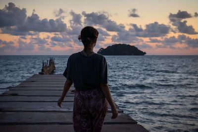 Rear view of woman standing on beach against sky during sunset