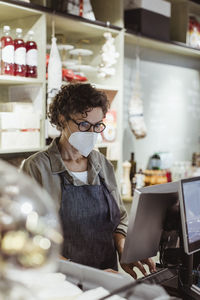 Female store owner working on computer in deli store during pandemic