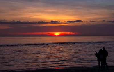 Silhouette people standing on beach against sky during sunset