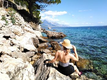 Rear view of woman sitting on rock by sea