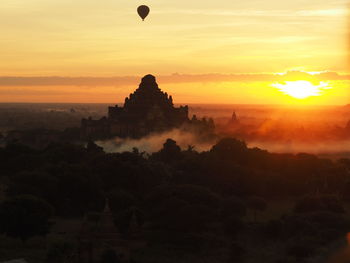 Silhouette hot air balloon over temple against orange sky during sunrise